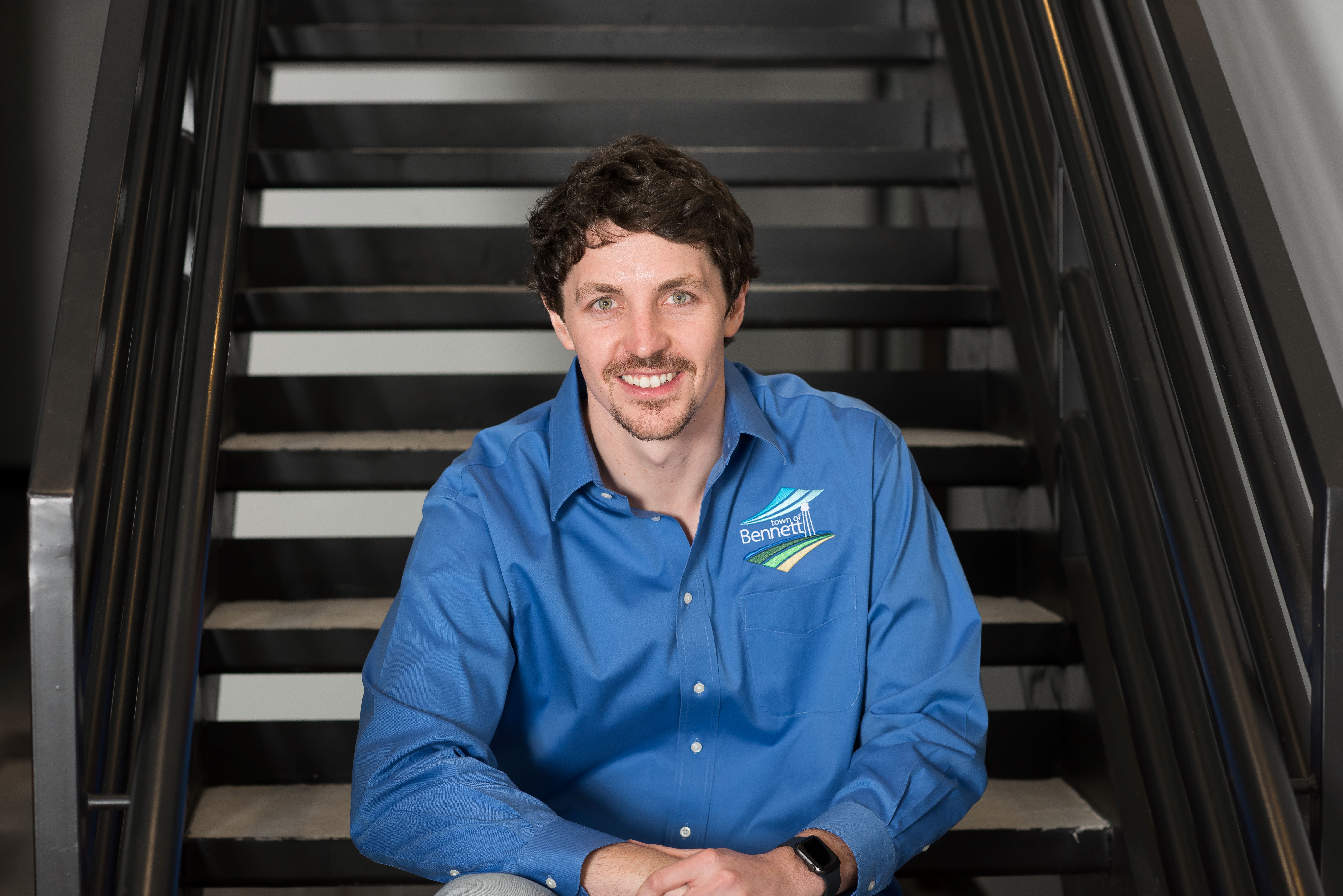 man with dark hair sitting on stairs wearing a blue shirt