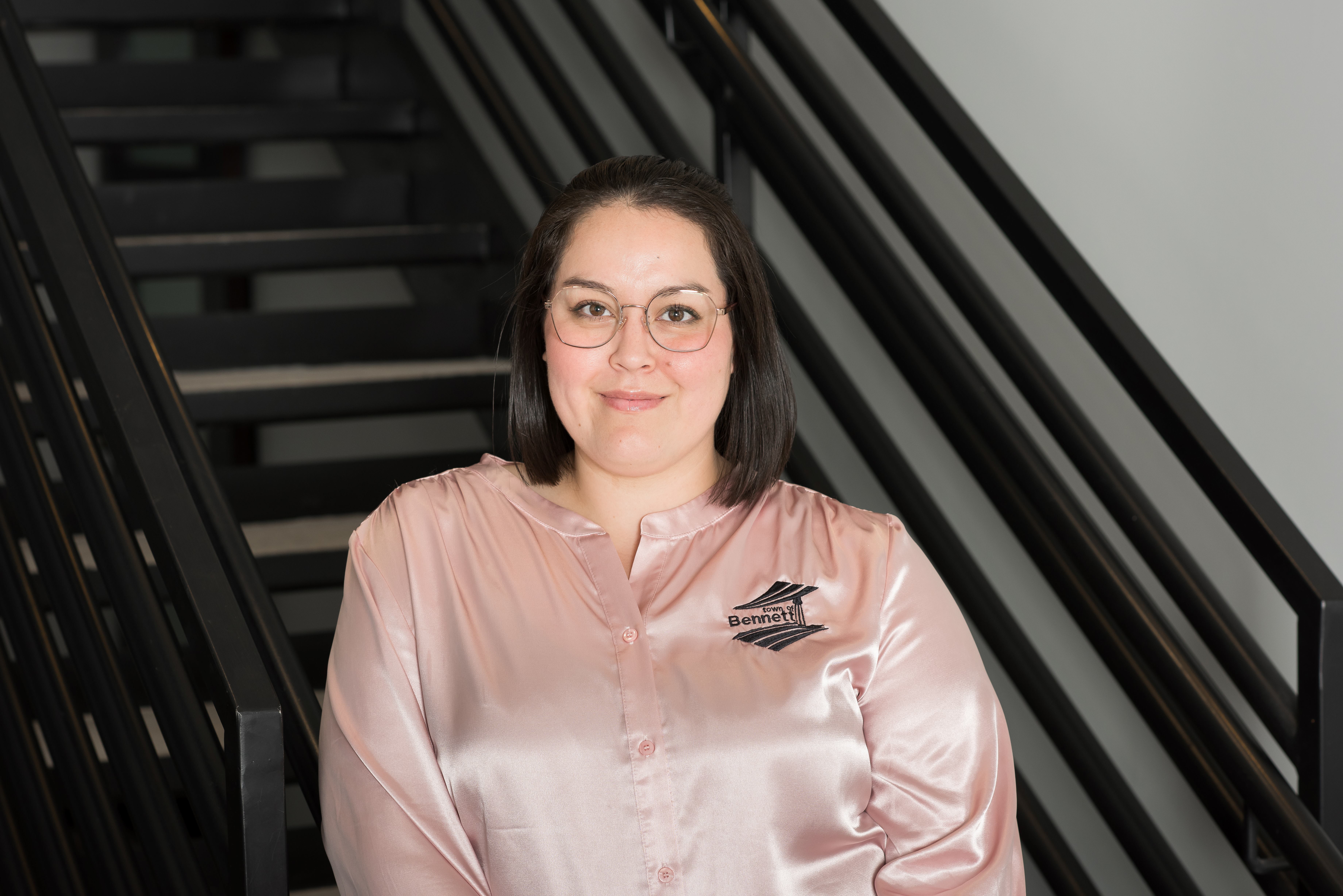 woman with glasses wearing a light pink shirt standing by stairs