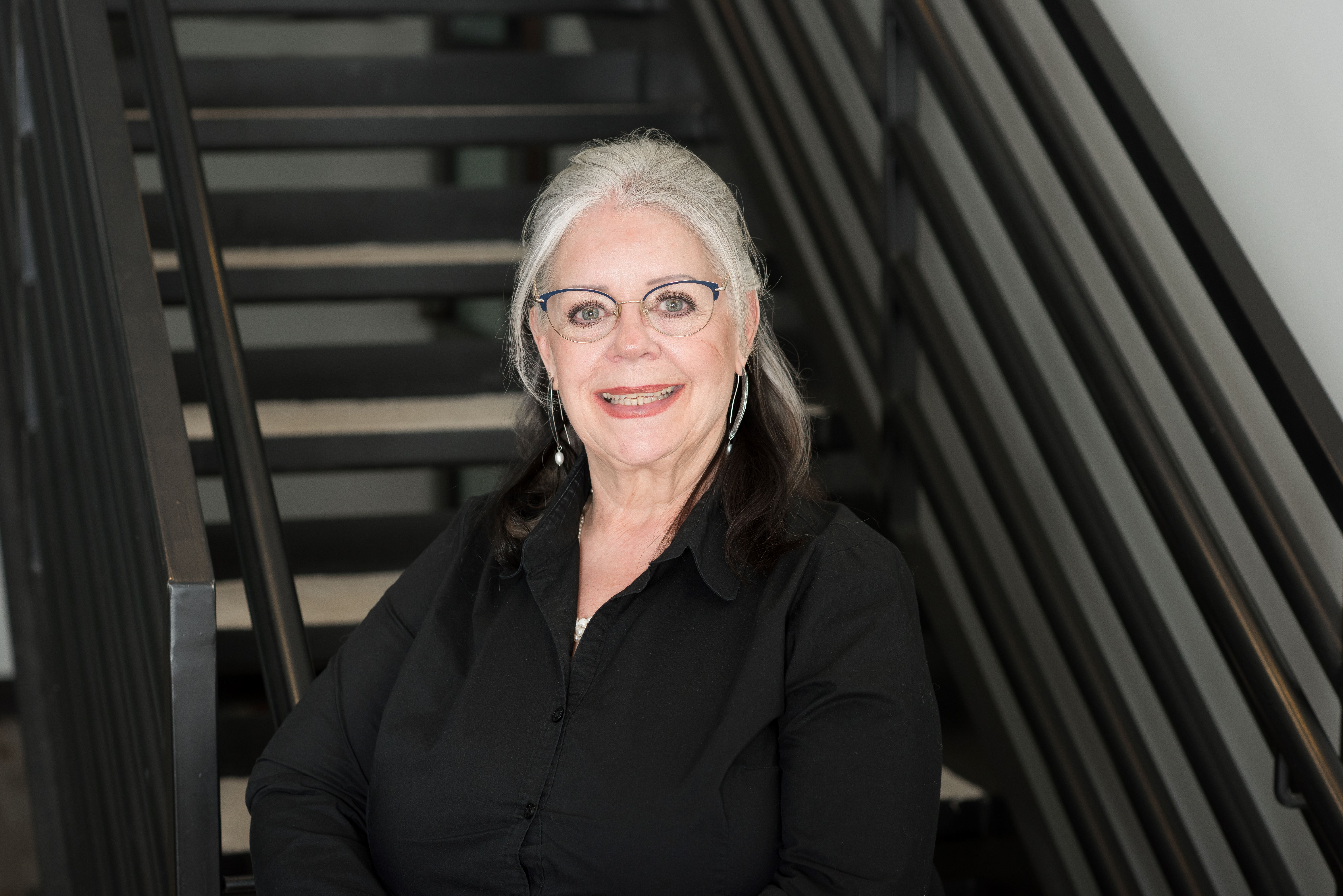 woman with glasses standing by stairs wearing a black shirt