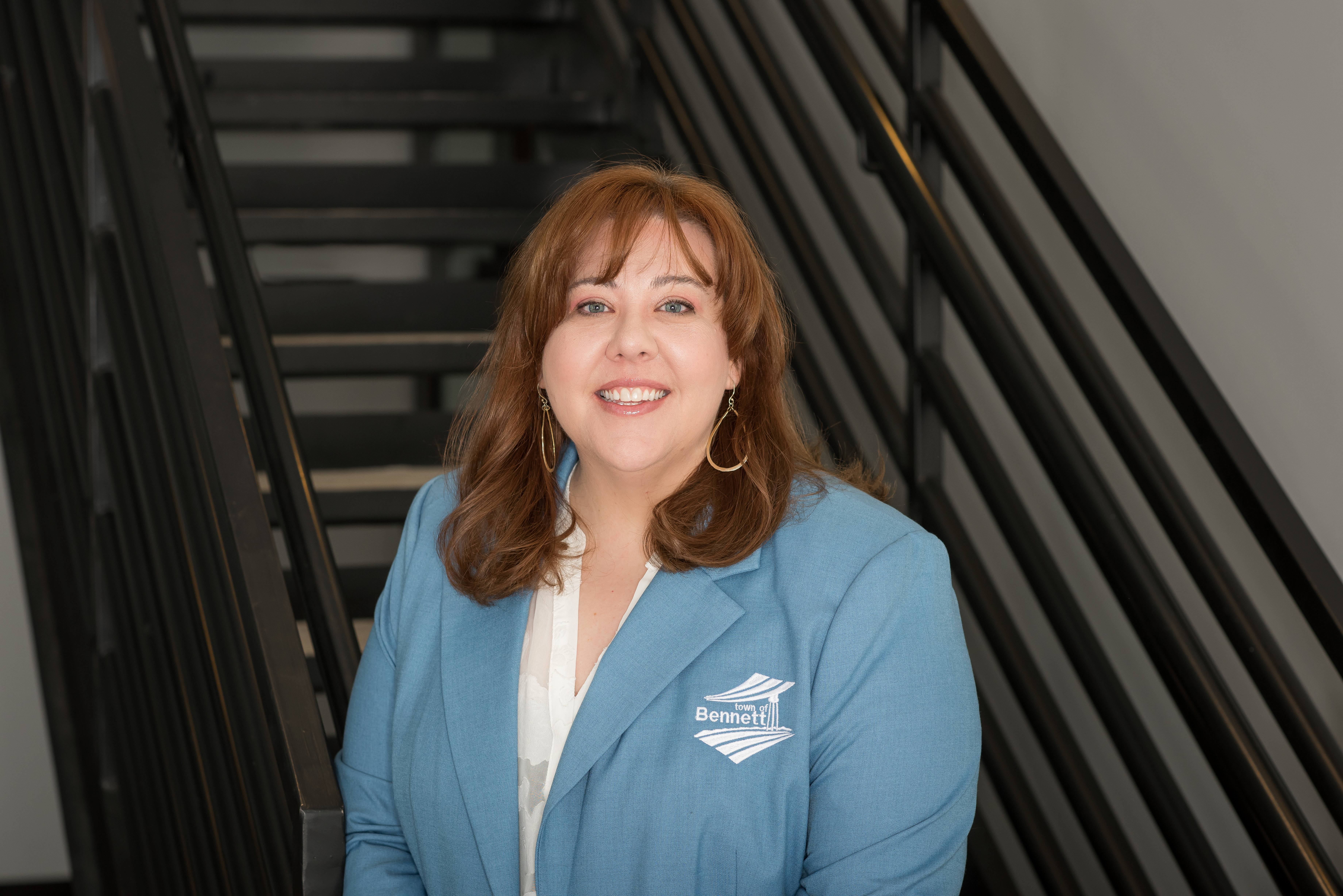 woman with brown hair standing by stairs in a light blue blazer