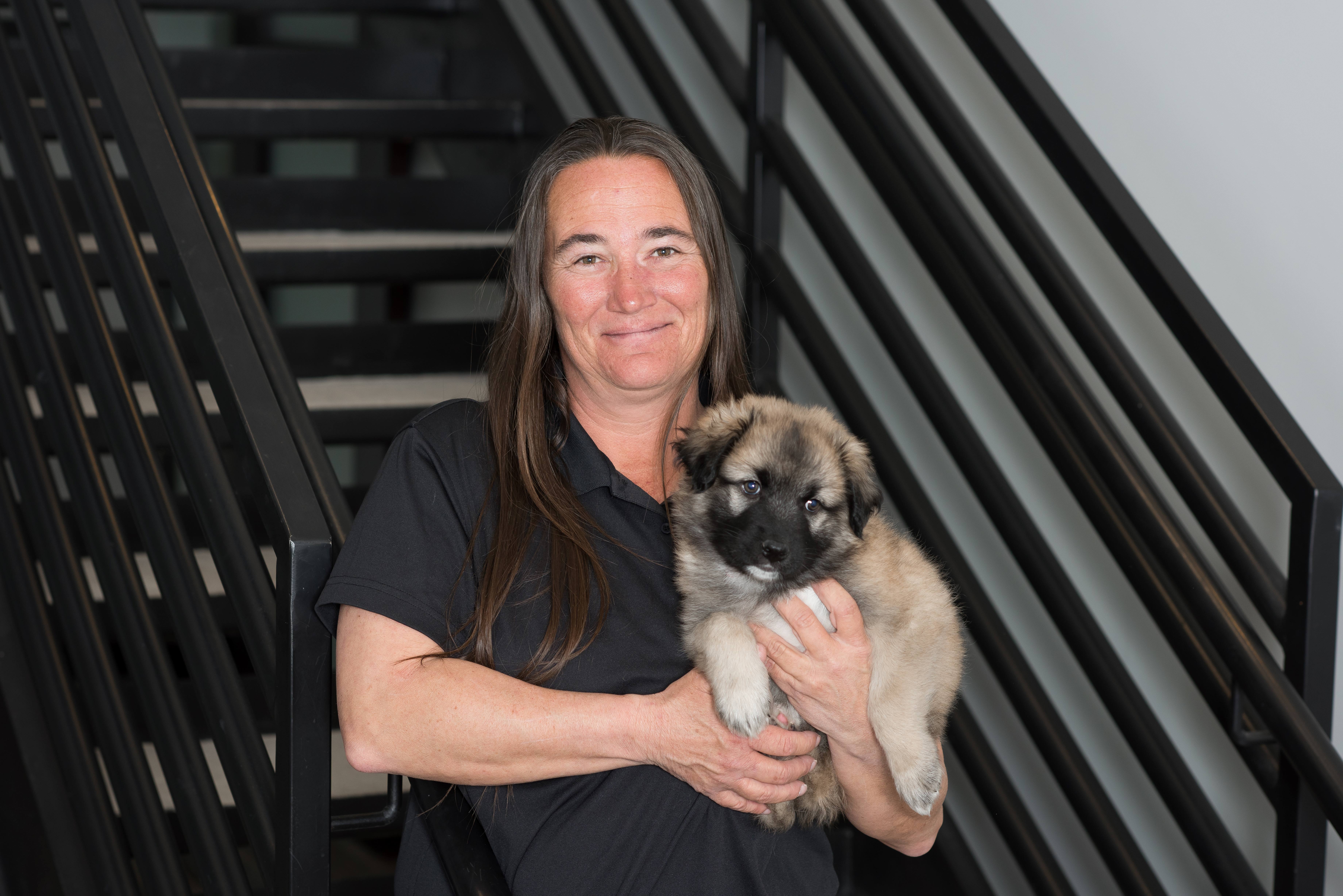 woman standing next to stairs holding a puppy and wearing a black shirt