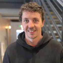 Photo of brunette male standing in front of a stairwell wearing a black sweatshirt