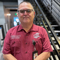 Photo of a man with grey hair in glasses and red shirt standing in front of stairs
