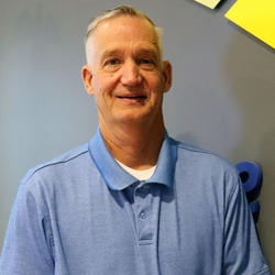 Trustee Steve Dambroski. Man standing in front of blue wall wearing a blue polo shirt. 
