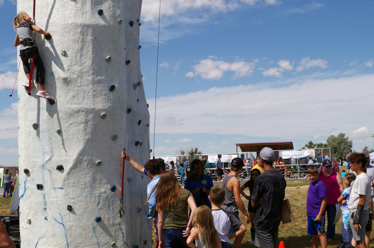 Child climbing a rock wall and people waiting in line at Bennett Days