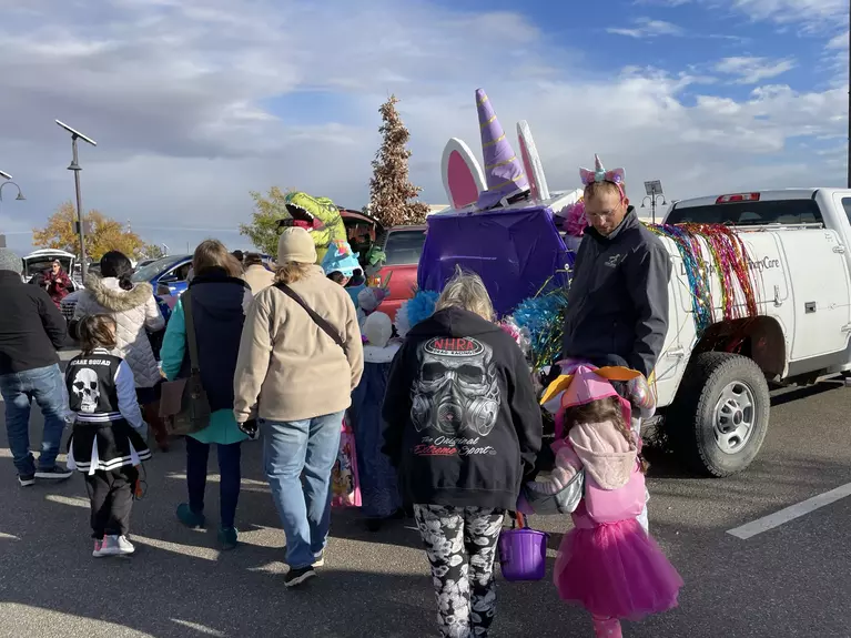 Adults and children outside walking by a white truck decorated for the trunk or treat event.
